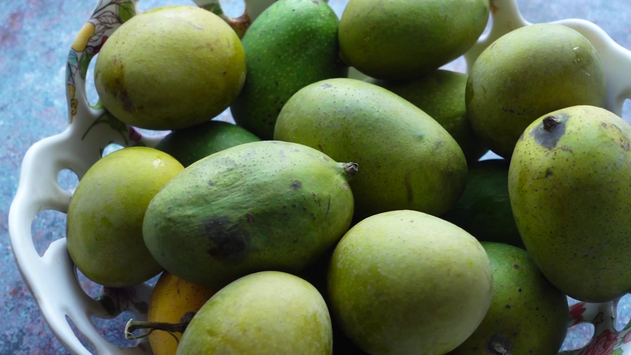 Mangas verdes frescas empilhadas em uma tigela branca.