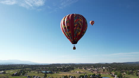 Vista-Aérea,-Globos-Aerostáticos-Volando-Bajo-Un-Cielo-Azul-Claro-Sobre-Un-Paisaje-Verde