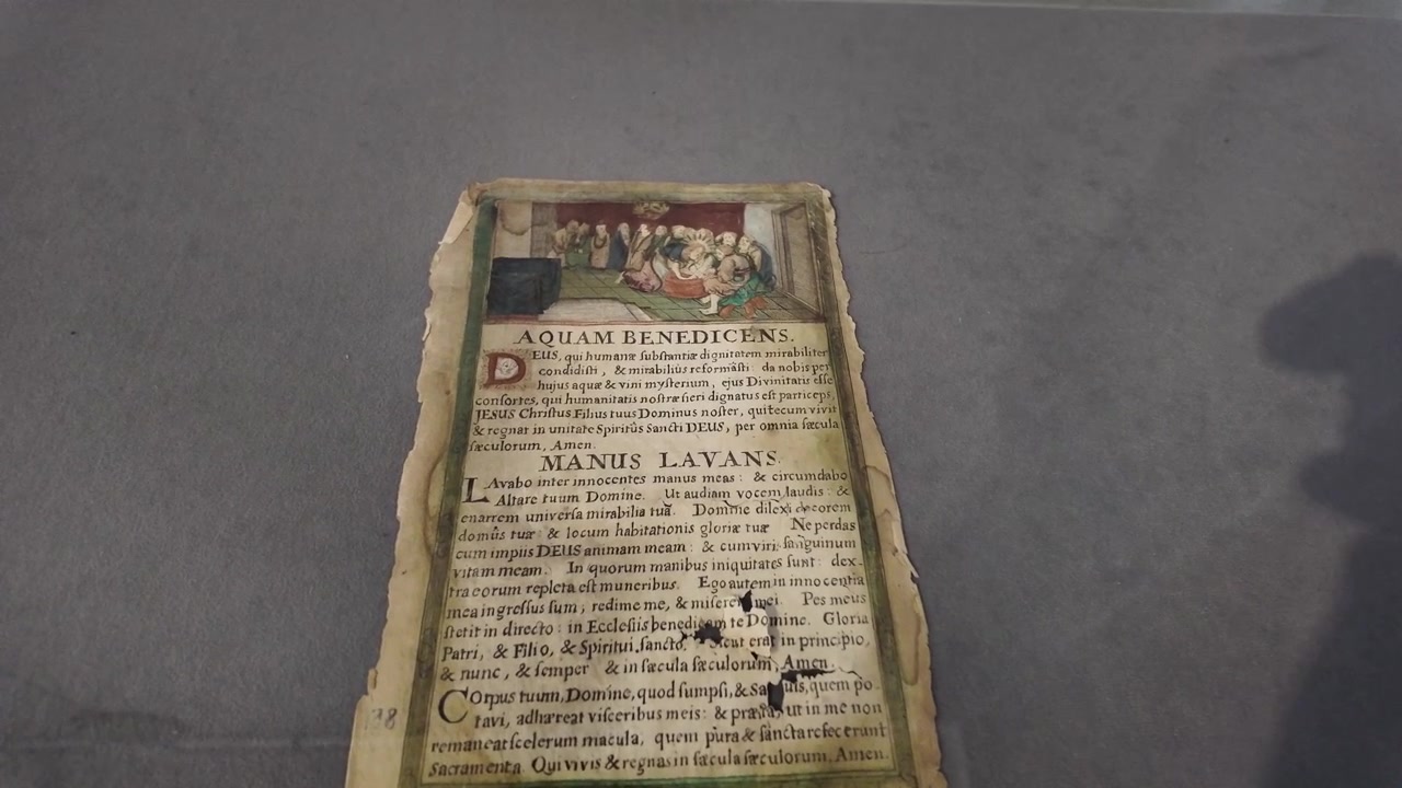 Pergamena medievale con bordi intricati, opere d'arte vivide e una scrittura elegante che fa riferimento alla benedizione dell'acqua.