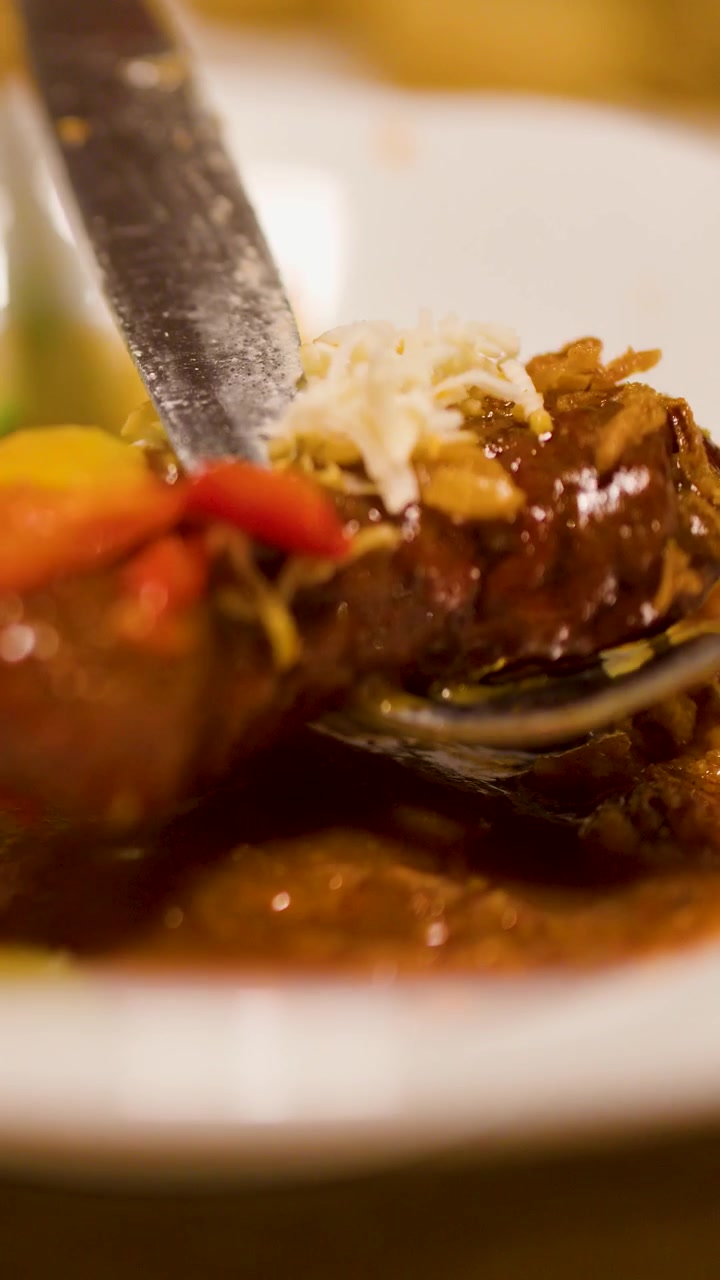 Un cucchiaio solleva un sostanzioso gulasch ceco con verdure e formaggio in un ambiente caldo di ristorante.