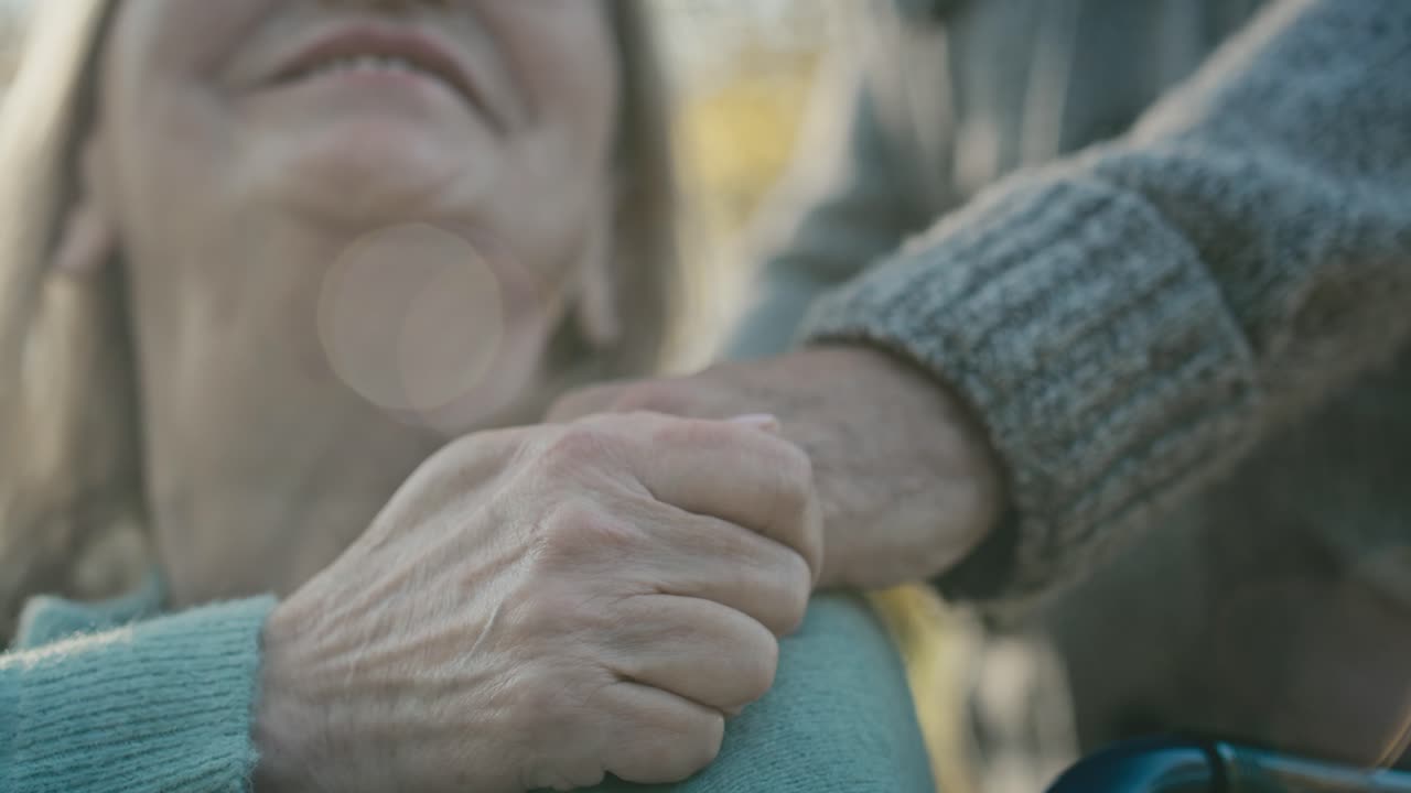 cerca del hombre tocando la mano de su esposa que está sentada en silla de ruedas