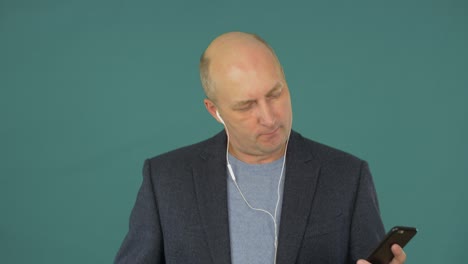 bald middle aged businessman listening music with earphones and smartphone