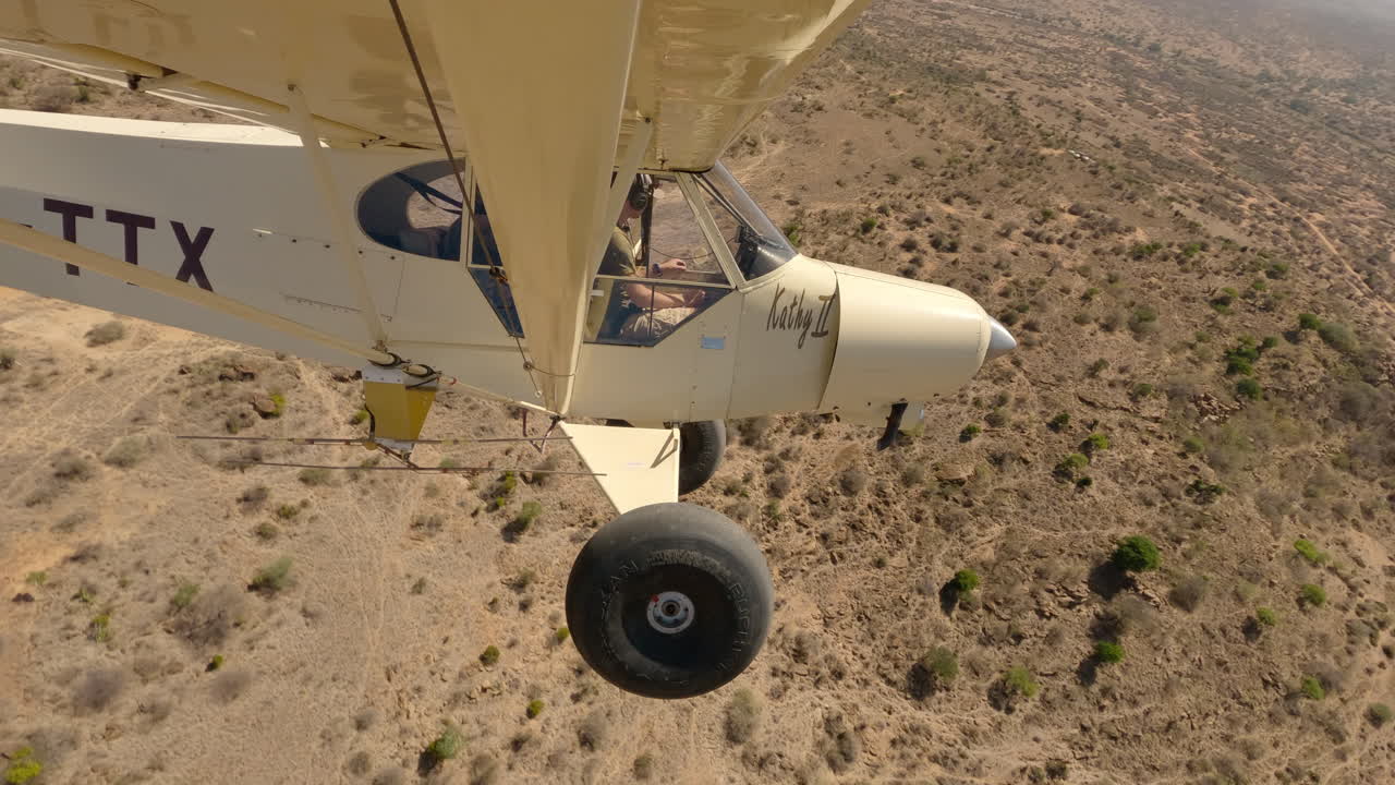 Pequeno Avião Leve Voando sobre um Leito de Rio em uma Planície Queniana