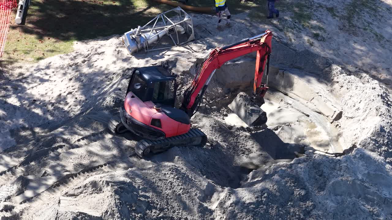 Un escavatore rosso scava sabbia in un cantiere edile su una spiaggia soleggiata a Gold Coast, Australia.