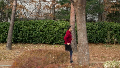 Vista-Lateral-Del-Hombre-De-Mediana-Edad-Corriendo-En-Un-Parque-Alrededor-De-Un-Apartamento-Moderno-En-Otoño