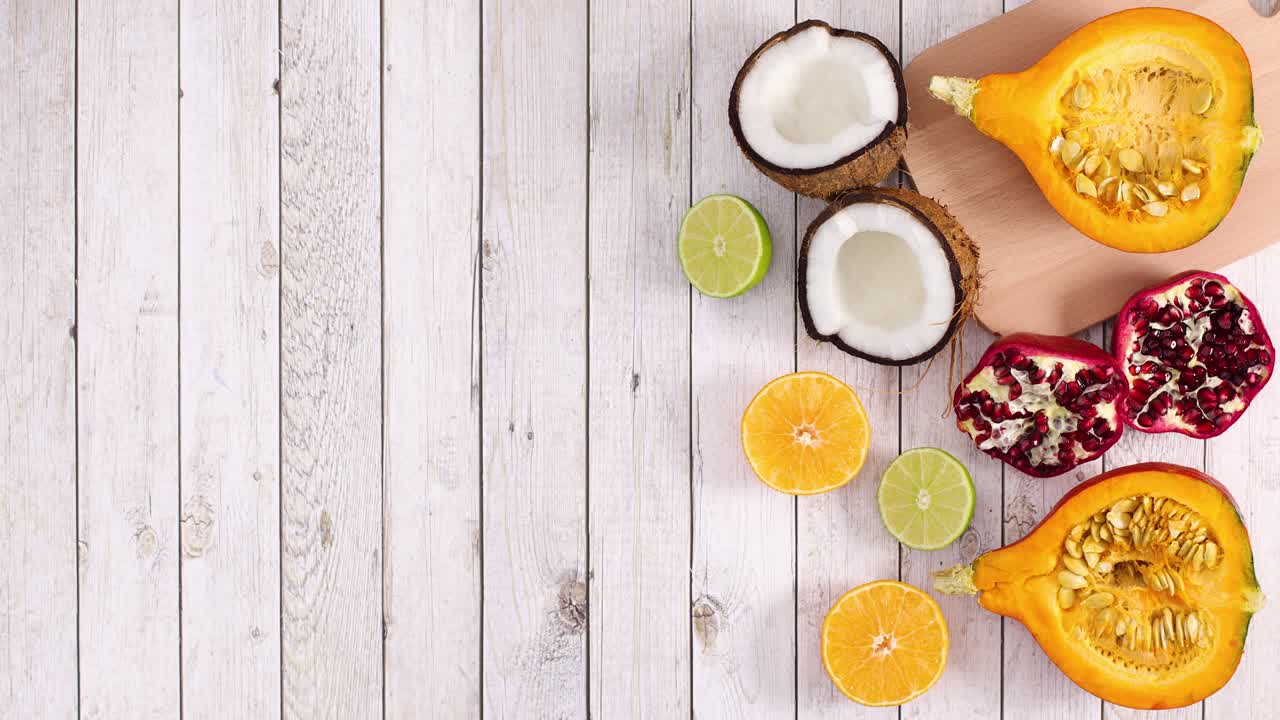 Frutta tropicale e agrumi maturi a fette appaiono sul lato destro di uno sfondo di legno chiaro. Stop motion