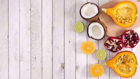 sliced ripe tropic and citrus fruits appear on right side of light wooden theme. stop motion