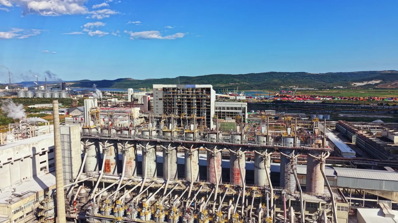 Sito industriale con macchinari ed edifici vicino a un fiume sotto un cielo azzurro brillante