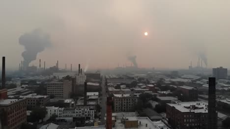 aerial view of industrial smokestacks under hazy sky at sunset, revealing urban landscape dominated by pollution and factory emissions