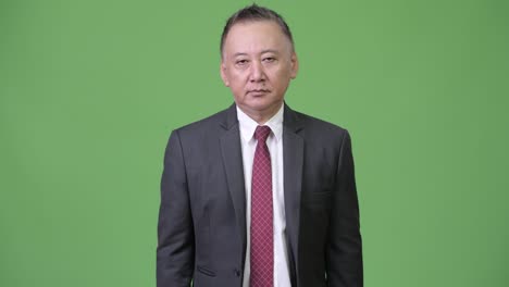 mature tired japanese businessman giving handshake against green background