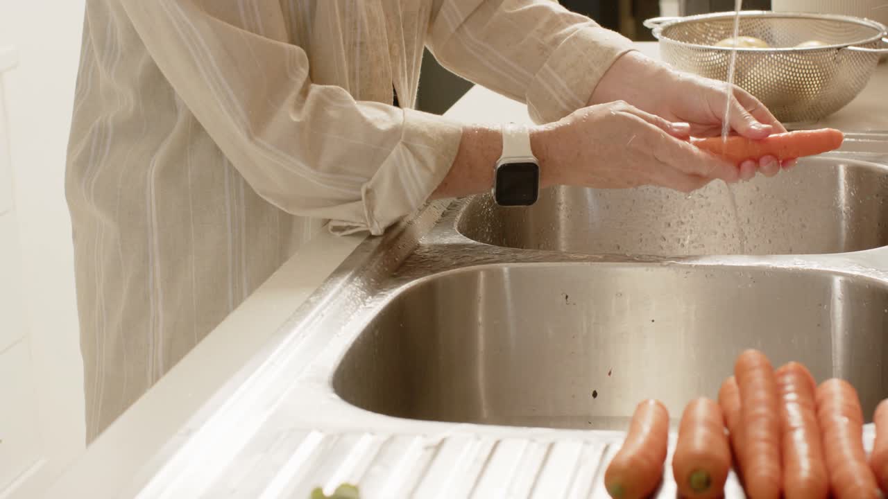 Femme adulte en blouse lavant des carottes à l'évier avec le robinet qui coule, dans une passoire, pour la préparation des repas.