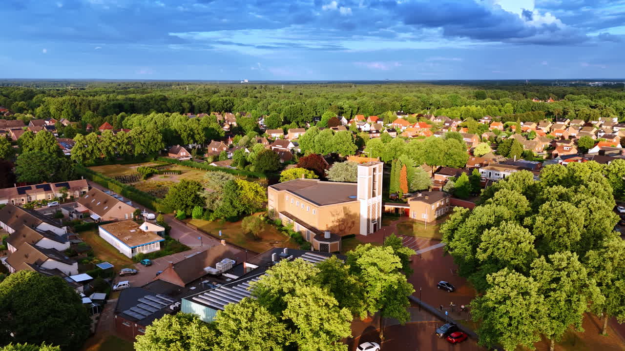Luftaufnahme eines Wohnviertels mit Kirche und Wald. Hochwinkel-Drohnenaufnahme von Vorstadthäusern, zentralem Kirchengebäude, grünen Bäumen und fernem Horizont unter blauem Himmel.