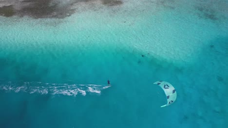 Kite-surfer-gliding-over-crystal-clear-turquoise-ocean,-aerial-view