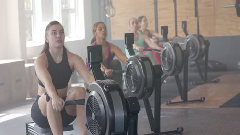 focused unaltered diverse women exercising on rowing machines at gym, in slow motion