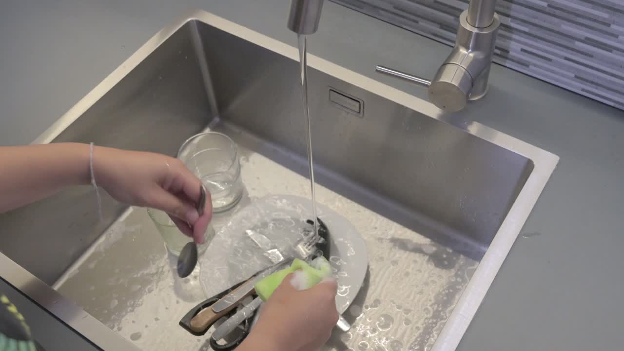 lavar cubiertos con una esponja en un fregadero de la cocina