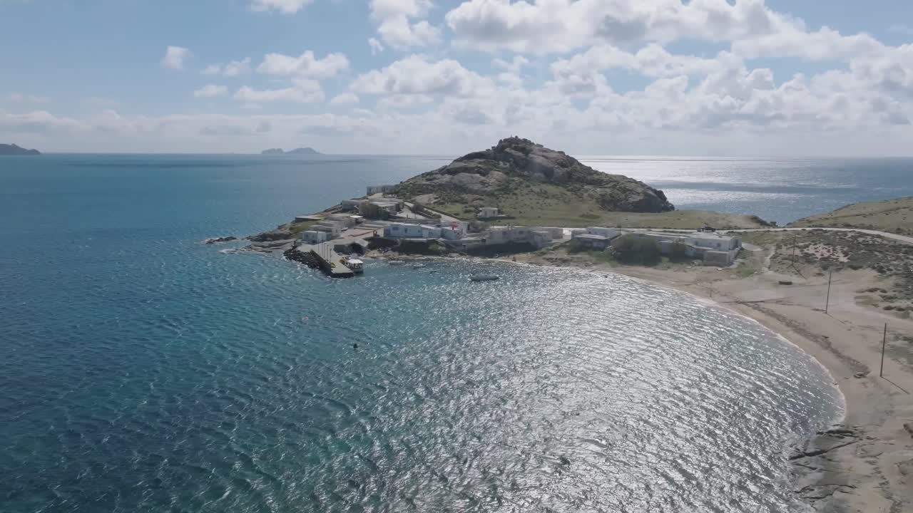 A cinematic drone shot of Divounia Beach in Mykonos, showcasing the traditional fishing village from an alternative perspective by the Aegean Sea