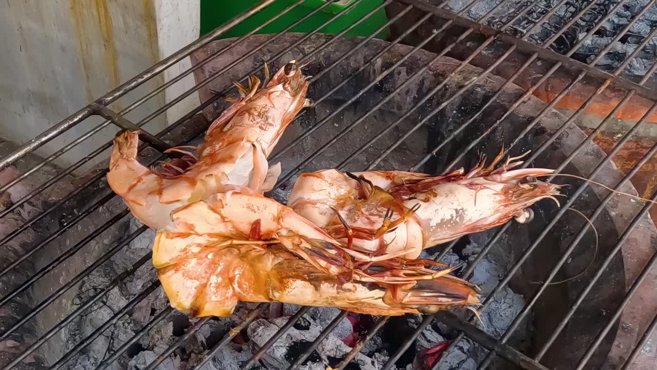 Detailed view of shrimp being grilled on a metal rack over glowing embers.