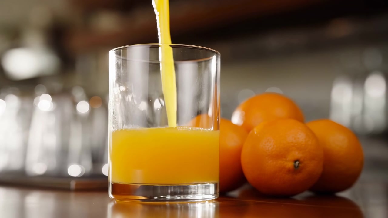 Sunlit Orange Juice Pouring Into Glass, Closeup Showing Citrus Pulp And Splashes, Ripe Oranges On Wooden