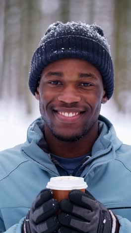smiling young afro man with a cup of hot coffee in a snowy forest