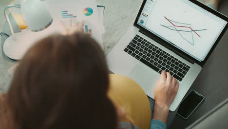 top view of pregnant businesswoman checking graphic chart on laptop at home.