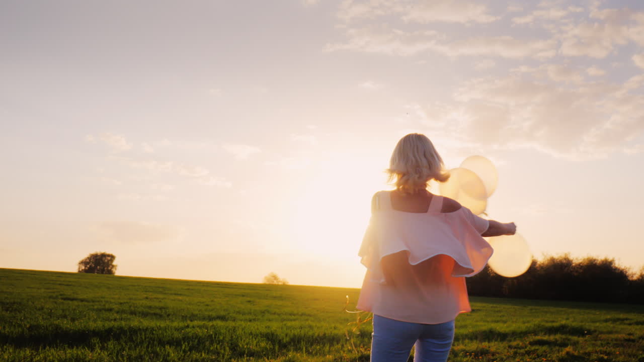 일몰 1에 녹색 초원을 걷는 풍선과 함께 평온한 젊은 여성