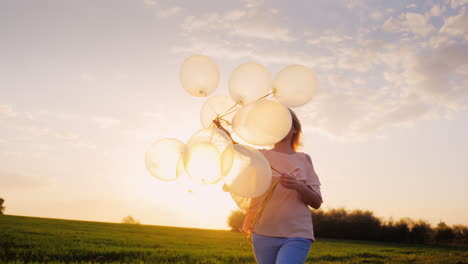 carefree young woman with balloons walking on a green meadow at sunset 1