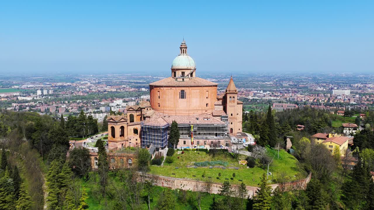 Aerial orbit shot of the Sanctuary of San Luca in Bologna, Italy, showcasing the iconic church atop a green hill with the city sprawling in the background
