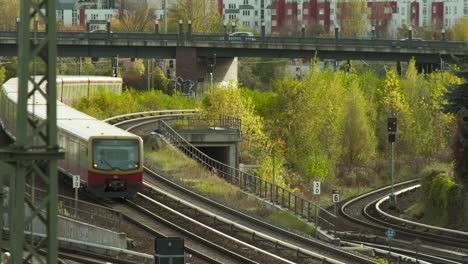 Tren-Rojo-De-La-Ciudad-Curvándose-En-La-Vía-Con-Fondo-Urbano