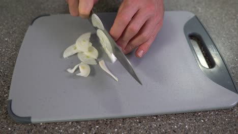 table top view - man hands, cutting white onion with chefs knife on grey chopping board