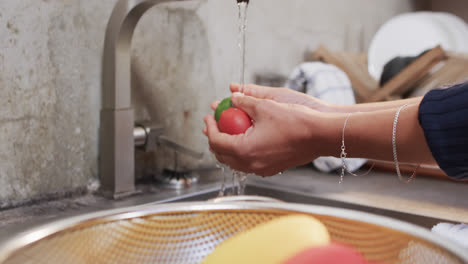 las manos de una mujer biracial enjuagando verduras en la cocina, en cámara lenta.