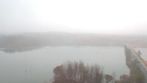 flying-backwards-over-a-foggy-lake-beside-a-road