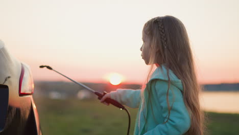 kid washes car with water spray on river grassland at dusk concentrated preschooler girl pours clear