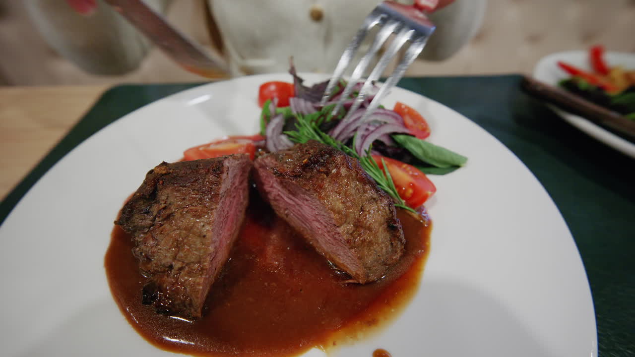 Primo piano di mani che tagliano un piatto di carne cotta con forchetta e coltello
