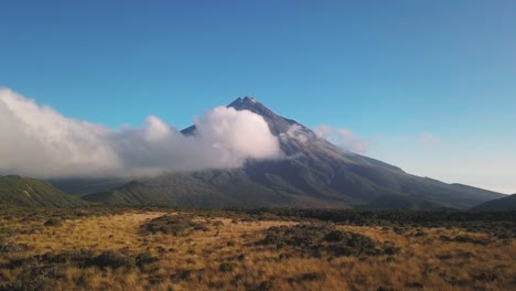 Volando-A-Través-De-Un-Campo-Hacia-Una-Montaña-Que-Está-Parcialmente-Envuelta-En-Una-Espesa-Nube-Blanca