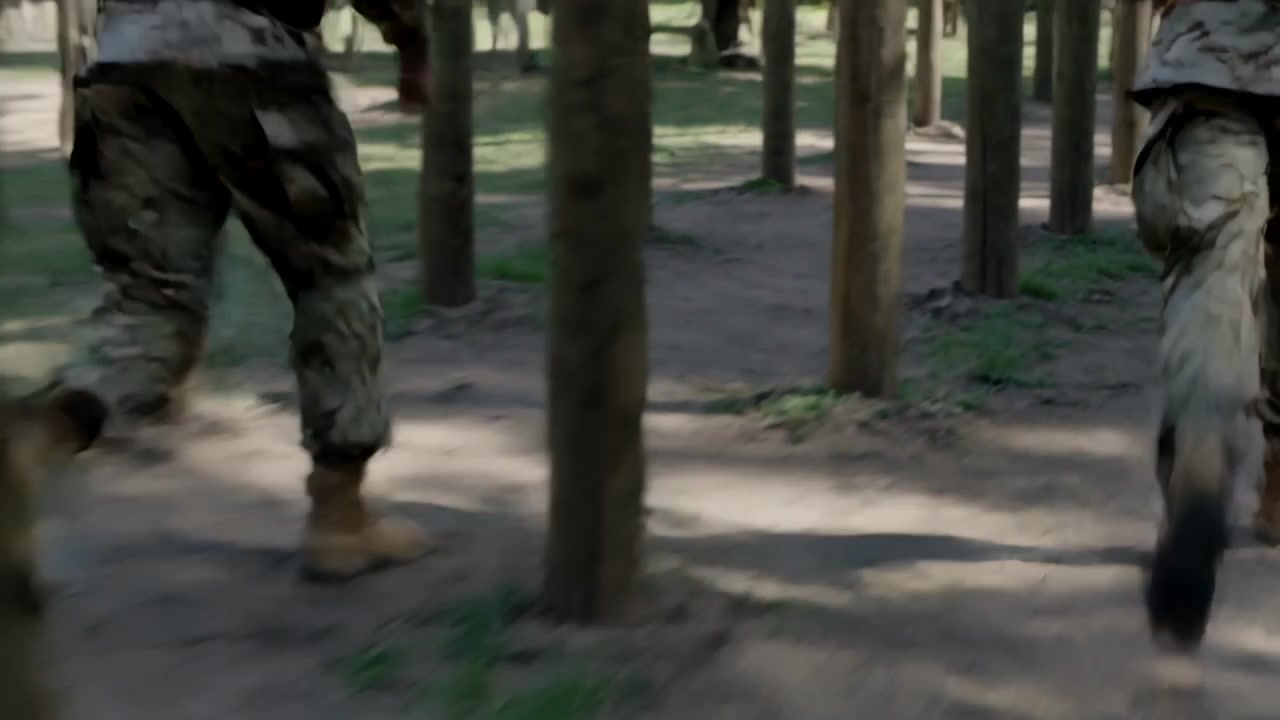 Entering left, two soldiers wearing camo pants and boots weaving through posts in training course