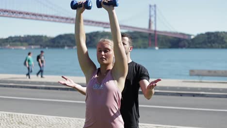 concentrated blonde woman exercising with dumbbells in park.