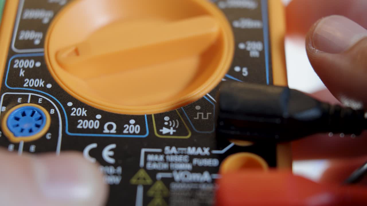 멀티미터를 사용하는 사람의 클로즈업, 전압, 전류, 저항 및 연속성과 같은 전기적 특성을 측정하는 다재다능한 도구, 정밀성과 기술적 전문 지식을 보여줍니다.