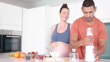 making smoothie, pregnant woman and partner blending fruits in kitchen, copy space