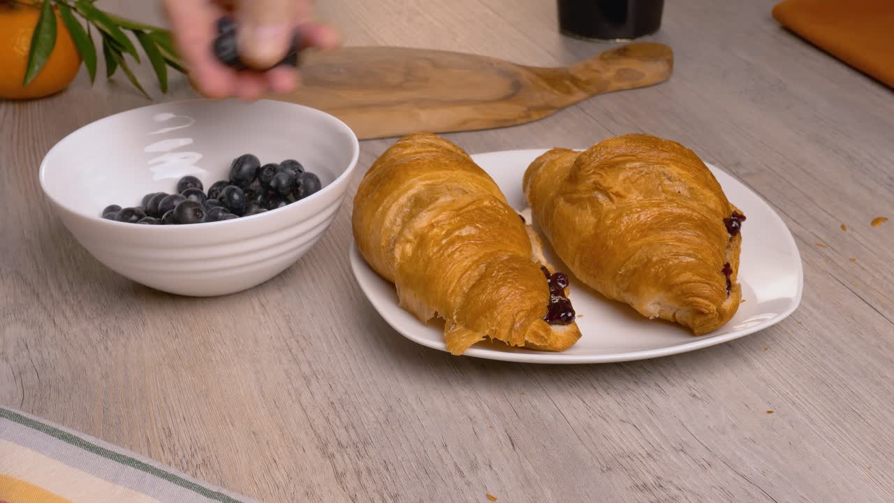 한 남자가 크로아산과 함께 접시에 신선한 블루베리를 놓습니다.