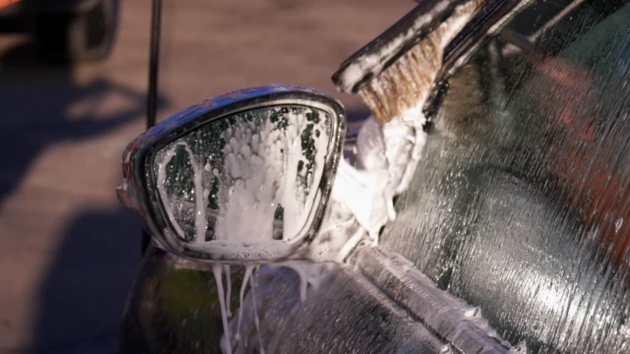A close-up of a car being washed with soap and a brush