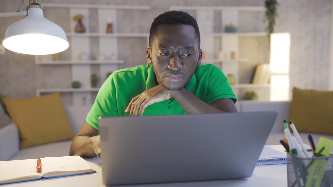 Black african man working in home office working thoughtful and focused using laptop.