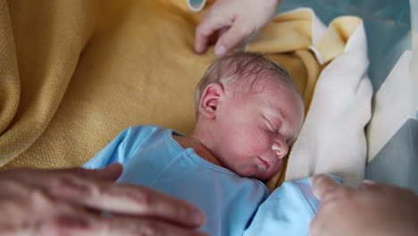 cute tiny baby boy few hours old sleeping in the crib. hands of loving parents caressing the child and he's smiling.