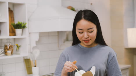 カメラを見て笑顔を振りながら持ち帰りラーメンを食べる幸せな日本人の女の子