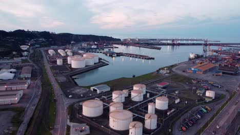 Vista-Aérea-Del-Puerto-Comercial-De-La-Ciudad-De-Gijón-Al-Norte-De-España,-Importación-Y-Exportación-De-Mercancías-Con-Contenedor,-Puesta-De-Sol-Iluminada-Al-Atardecer