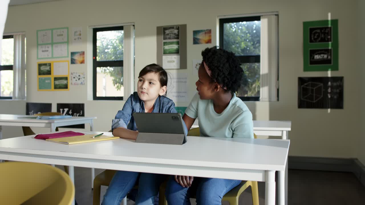 Two preteen classmates watching tablet in class reacting to teacher appearing, working with notes