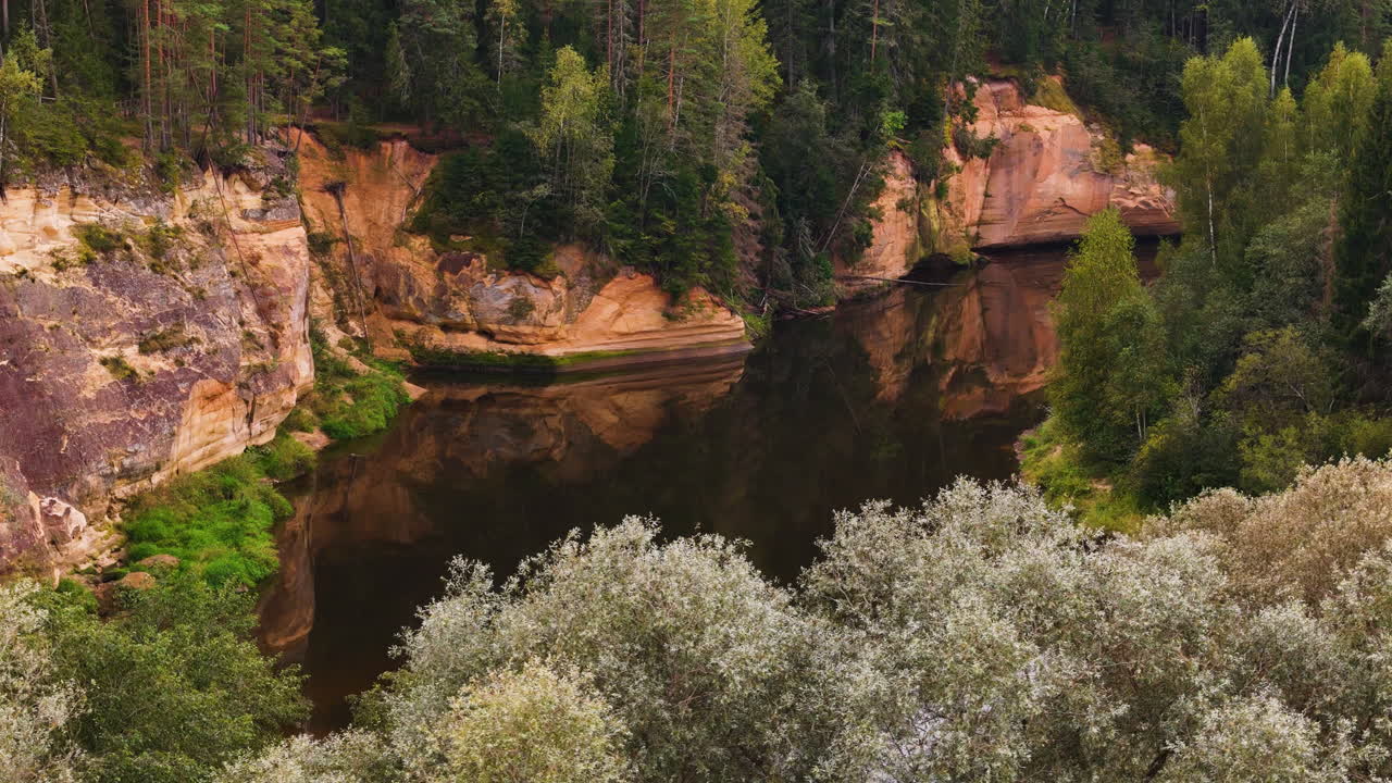 Breathtaking aerial footage of Erglu Ergelu Klintis, Latvia, showcasing striking sandstone cliffs, a reflective river, and lush forest.