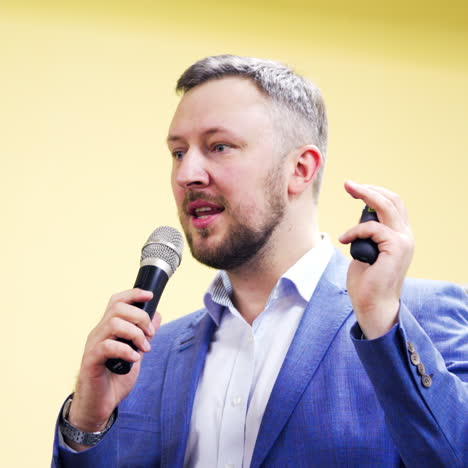professional educator in white shirt and blue suit speaking into the microphone in the business forum. handsome man speaker conducting a lecture. close-up
