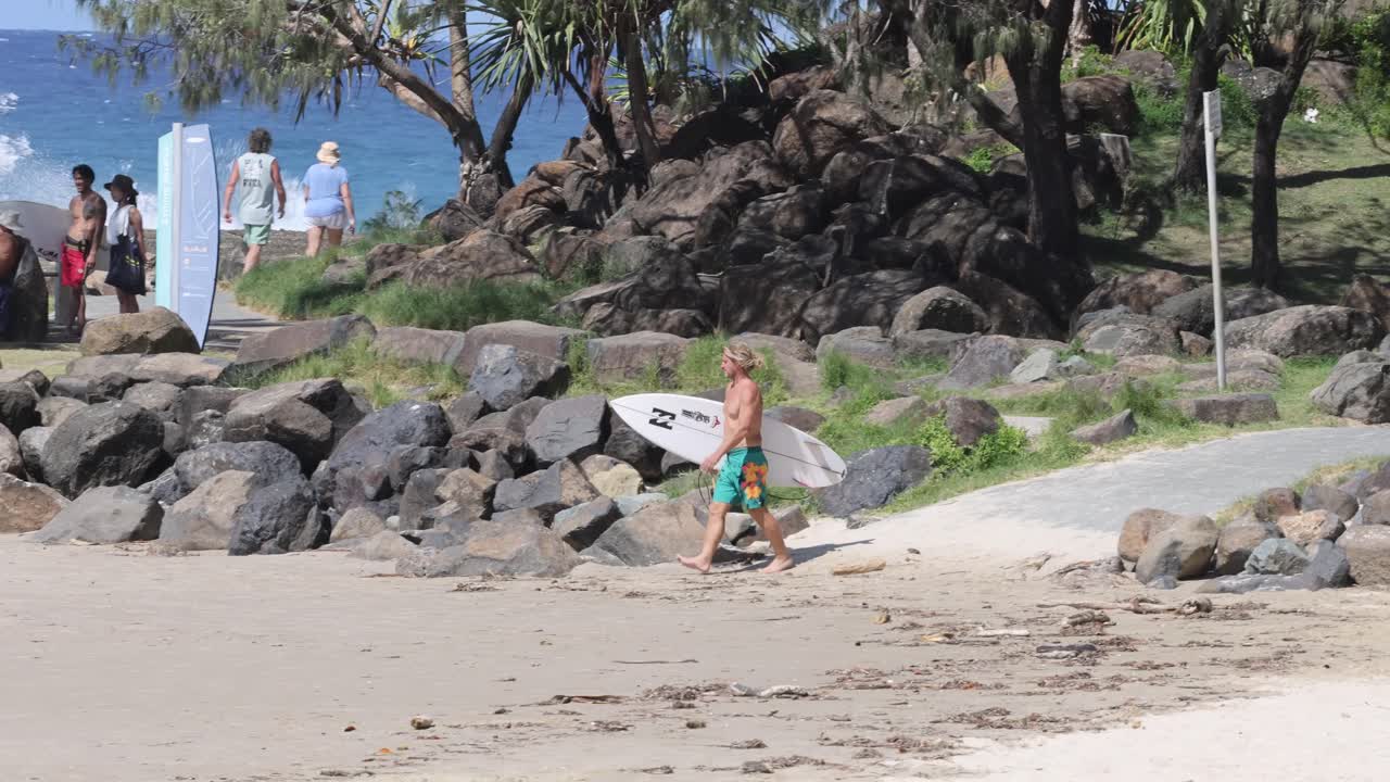 серфер несет доску вдоль живописной пляжной тропы