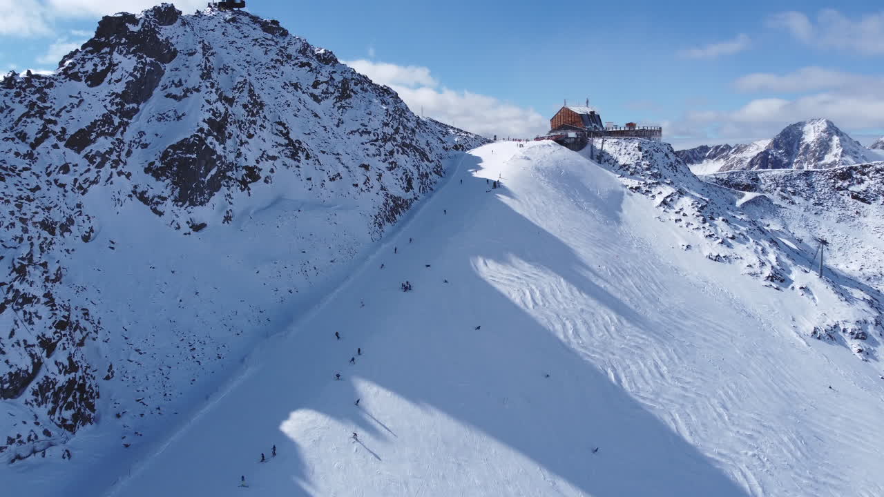 toma aérea que asciende por encima de una pista de esquí popular para revelar la vista panorámica más hermosa y pintoresca de los picos montañosos nevados circundantes, el glaciar val senales, tirol, italia