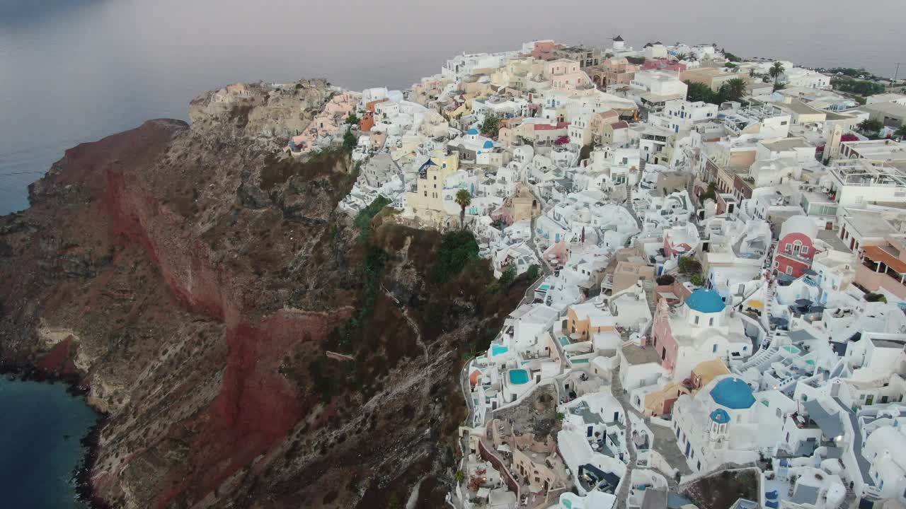 vista de avión no tripulado en grecia volando sobre santorini con la ciudad de oia casas blancas y techos azules en un acantilado junto al mar mediterráneo al amanecer